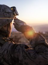 A soldier in full combat gear salutes the sunrise.